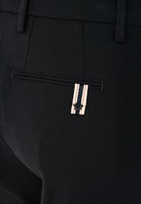 Czarna materiałowa para spodni z tylną kieszenią z małą metką w kremowe, granatowe i czerwone paski oraz subtelnym teksturowanym wykończeniem.