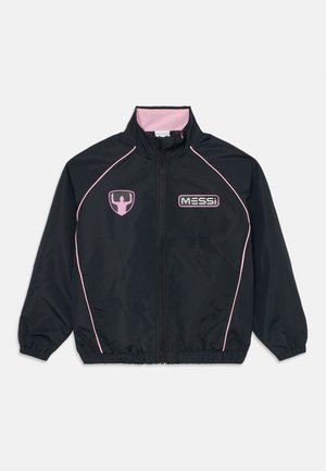 Musta vetoketjullinen urheilujacke pinkeillä yksityiskohdilla, pinkki sisäkaulus, "MESSI" logo oikeassa rinnassa ja kohotettu käsien siluetti -embleemi vasemmassa rinnassa.