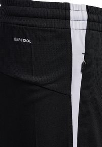 Shorts deportivos negros hechos de una tela transpirable, con una franja lateral blanca y un pequeño bolsillo con cremallera que lleva una etiqueta de marca.