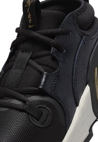 Scarpa da atletica Nike con tomaia in rete nera testurizzata, accenti lisci in blu navy, lacci a corda e un'intersuola bianca con un dettaglio dorato del logo.