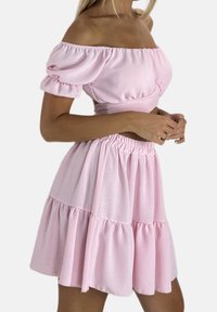 Roze off-shoulder jurk gemaakt van zachte stof, met pofmouwen, een aansluitend lijfje en een gelaagde, geplooide rok.