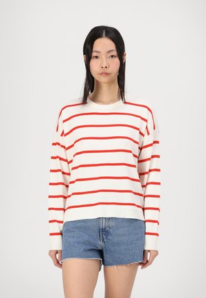 Rød og hvit stripete genser med rund hals, senkede skuldre og ribbestrikkede mansjetter, paret med lyseblå denimshorts.
