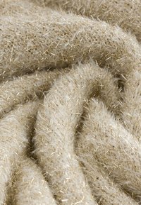 Beiger, strukturierter Stoff mit flauschigen Fasern, durchsetzt mit goldenen Strängen, die ein weiches, schimmerndes Aussehen erzeugen.