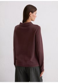 Bordeaux gebreide pullover met een hoge kraag en lange mouwen. Zachte textuur, minimale naden en een ontspannen pasvorm, gecombineerd met grijze broek.