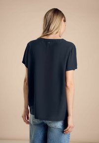 Top corto grigio scuro a maniche corte con scollo rotondo, caratterizzato da un dettaglio a bottoni sulla schiena e una vestibilità morbida, realizzato in un tessuto liscio.