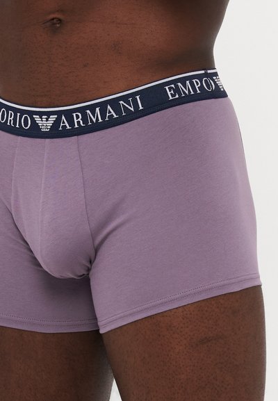Lila bombažna bokserica z zmogljivo temno modro elastično pasom, na katerem je v belem napisu "Emporio Armani". Gladka tekstura, prilegajoča se zasnova.