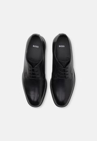 Black leather dress shoes with a smooth texture, lace-up design, and a rounded toe. "BOSS" logo appears on the insoles.