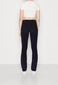 Donkerblauwe flared corduroy broek met een zachte textuur, vijf zakken en een hoge taille, gecombineerd met een cropped wit topje.