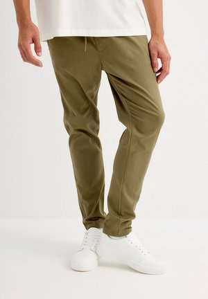 Pantalones verde oliva con corte slim, que cuentan con una cinturilla elástica y una textura suave, combinados con zapatillas blancas.