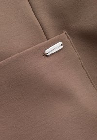 Braun strukturierten Stoff mit einem sichtbaren silbernen Etikett mit der Aufschrift "QUINTESSENCE". Der Stoff ist glatt und hat ein dezentes Webmuster.