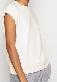 Top de manga corta en crema hecho de tela suave, con cuello acanalado y corte relajado que cae a la altura de la cintura.