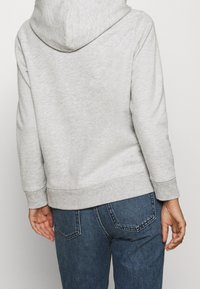 Sudadera de algodón gris con capucha, con un corte holgado, puños acanalados y dobladillo, combinada con jeans de mezclilla azul oscuro.