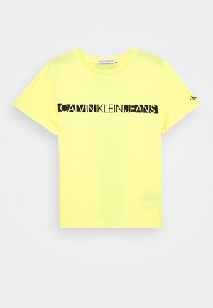 T-shirt jaune vif à manches courtes en coton. Présente un logo noir "CALVIN KLEIN JEANS" imprimé sur le devant. Encolure ras du cou classique.
