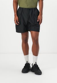 Black shorts made of lightweight fabric, featuring an elastic waistband, side zip pockets, and a relaxed fit. Worn with grey socks and black shoes.