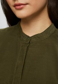Camicia in corduroy verde oliva con colletto rotondo e chiusura a bottone, caratterizzata da una superficie testurizzata e dettagli a costine verticali.