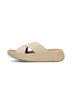 Beige slip-on sandaal met kruisbandjes en dikke gevlochten plateauzool, zijaanzicht op witte achtergrond.