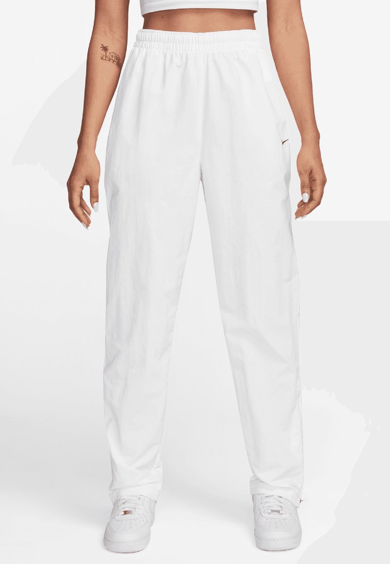 Pantaloni jogger bianchi, leggeri, con vita elasticizzata, tasche laterali e un dettaglio di marca vicino alla tasca. Texture liscia.