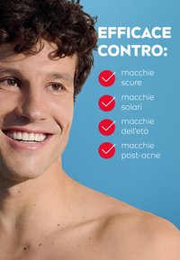 Primo piano di una persona sorridente con capelli ricci e scuri, su uno sfondo blu. Il testo elenca le preoccupazioni della pelle: macchie scure, macchie solari, macchie dell'età, post-acne.