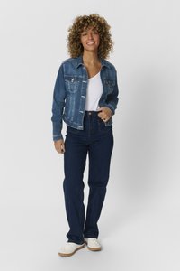 Chaqueta de mezclilla en azul medio con cierre de botones, dos bolsillos en el pecho, combinada con vaqueros azul oscuro y zapatillas blancas. Textura suave.