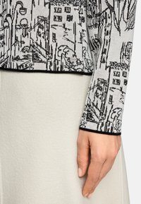 Knit sweater with a monochrome cityscape design, featuring a black and white color scheme and black cuffs. Smooth, textured fabric against a light skirt.