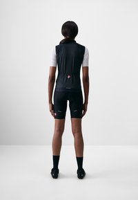 Svart ermeløs sykkelvest med en tettsittende design, brukt over en hvit kortermet skjorte, kombinert med svarte sykkelshorts og sko.