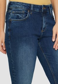 Dunkelblaue Denim-Jeans mit einer leichten Ausbleichung, fünf Taschen und goldenen Nähten. Der Stoff hat eine glatte Textur und ein figurbetontes Design.