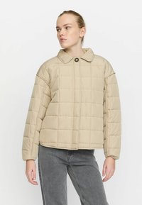 Beige quiltet pufferjakke med krave, frontknaplukning og brede ærmer, parret med grå bukser. Glat, letvægtsstof.