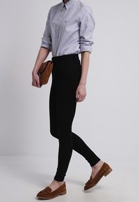 Randig skjorta i ljusblått och vitt, svarta skinande jeans, bruna mockaloafers och en brun clutchväska.