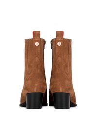 Botas de tobillo de ante marrón con un tacón cuadrado negro, que presentan un cierre de cremallera y acentos rojos, con un diseño de costura decorativa en los lados.