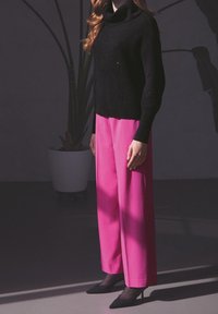 Suéter negro de cuello alto acanalado, pantalones amplios rosas, tacones negros de punta. Las texturas suaves y los colores en contraste crean un look audaz.