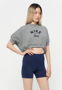 Sweatshirt cinzento cropped com "NIKE 1972" em preto, combinado com calções de cintura alta de cor azul-marinho. Tecido suave, casual e com ajuste descontraído.