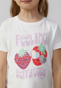 Witte T-shirt met een kleurrijke aardbeienafbeelding met glitter en een bril, harten en de tekst "Feeling Berry Good" in roze.