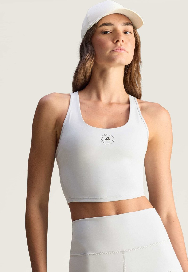 Valkoinen lyhyt urheilullinen toppi, jossa on pyöreä kaula-aukko ja huomaamaton logo. Sujuva kangas, istuva malli, yhdistetty korkeavyötäröisten vastaavien alaosien kanssa.