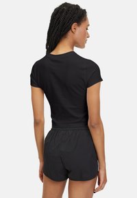 Zwart cropped top met korte mouwen, gemaakt van gladde stof, gecombineerd met zwarte shorts met elastische taille. Eenvoudig, gestroomlijnd ontwerp zonder zichtbare versieringen.