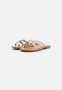Sandali piatti con diverse fibbie dorate, alcune con un motivo texture, su una suola marrone chiaro.