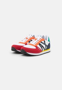 Ténis desportivos em vermelho, branco e azul-marinho com detalhes em laranja e amarelo. Feitos de camurça e malha, com atacadores planos e uma sola de borracha texturizada.