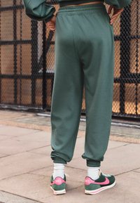 Grønne sweatpants med elastisk talje og manchetter, kombineret med grønne og pink Nike sneakers. Hvide sokker er synlige.