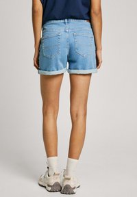 Denimshorts i ljusblått, med upprullade fållar, femficksdesign, hög midja, bakfickor med sömdetaljer, ihopparade med vita strumpor och sneakers.
