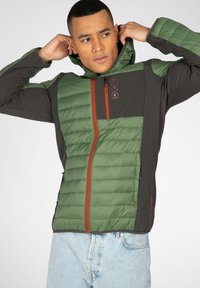 Giacca isolante verde e grigio scuro con cappuccio, parte frontale trapuntata, zip arancione a contrasto e dettaglio con logo sul petto.