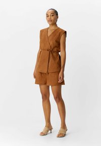 Ensemble en deux pièces en suede marron comprenant un top sans manches à nouer et un short assorti. Texture lisse, design décontracté.