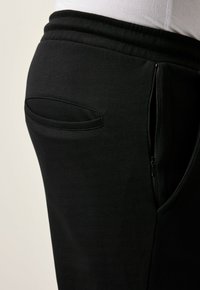 Pantalones de chándal negros con una textura suave, que cuentan con un bolsillo lateral con cremallera y una cintura elástica para un ajuste seguro.