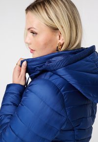 Blauwe pufferjack met een capuchon, met een gewatteerd ontwerp, een gladde textuur en zichtbare stiksels. Hoge kraag en trekkoorddetails.