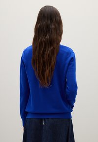 Blauwe gebreide trui met lange mouwen, ronde halslijn en geribbelde onderrand. Zachte textuur en aansluitende silhouette, gedragen over een donkere spijkerrok.