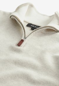 Cream-colored pullover with a half-zip design. Made from textured knit material, featuring a leather pull tab and ribbed collar. Brand label visible.