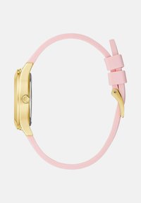 Kuldne kellakorpus roosa silikoonist rihmaga ja kuldse pandlaga, shown külgvaates lihtsa heleda tausta ees.