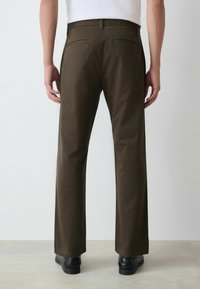 Brūni taisni bikses ar gludu tekstūru, ar divām aizmugures kabatām un klasisku jostu, apvienotas ar melniem apaviem.