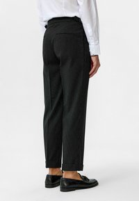 Zwarte broek met streepjes in een taps toelopende pasvorm, met omgeslagen uiteinden en details op de achterzak, gecombineerd met zwarte instappers.