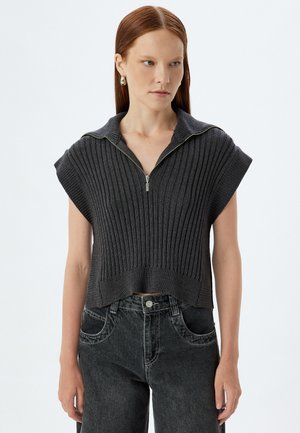 Donker, geribbelde gebreide cropped top met korte mouwen en een ritssluiting bij de kraag, gecombineerd met hooggetailleerde vervaagde zwarte jeans. Soepele textuur.