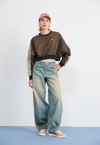 Korte zwarte sweatshirt met luipaardprint en witte strepen; vervaagde blauwe wijde jeans; beige en bruine sneakers met witte veters.