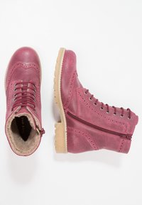 Růžové kožené kotníkové boty s brogue detaily, šněrováním vpředu, bočním zipem a béžovou gumovou podrážkou. Huňatá podšívka viditelná na otvoru.